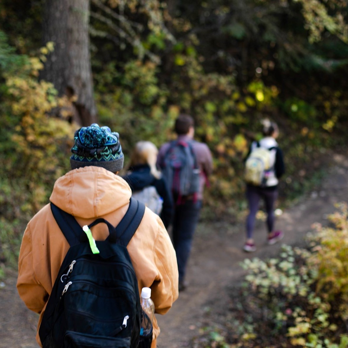 Student in orange jacket hiking on a trail